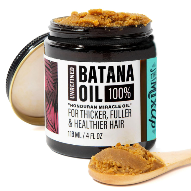 Jar of Batana Oil with a wooden spoonful of oil on a white background