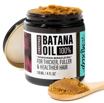 Jar of Batana Oil with a wooden spoonful of oil on a white background